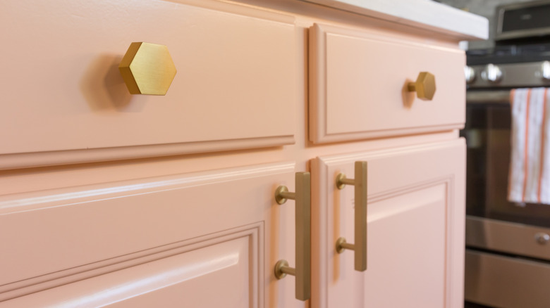 Gold drawer pulls and cabinet hardware are installed on salmon-colored kitchen cabinetry