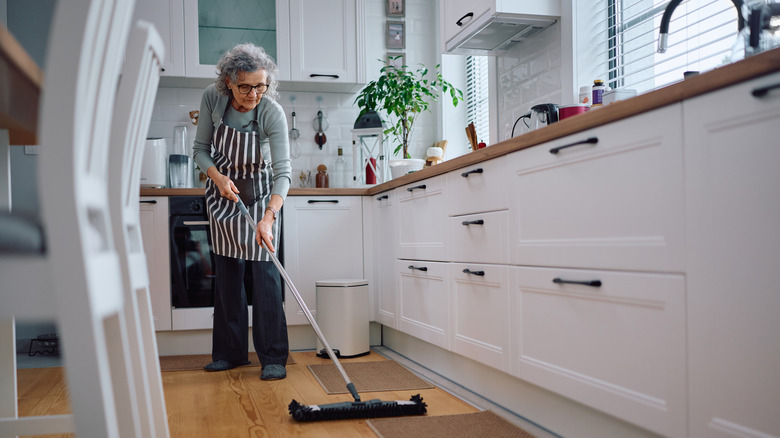 A woman uses a large mop to clean her kitchen floors