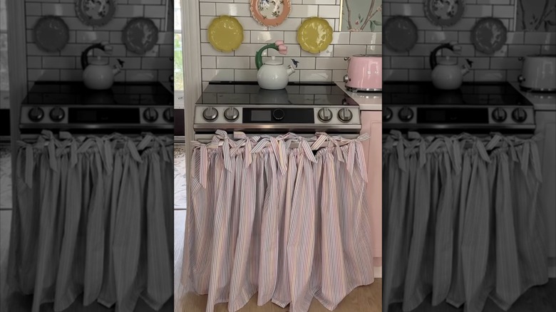 A pink oven curtain in a whimsical kitchen with pink cabinets, white subway tile backsplash, plates on the wall, and a pink Smeg toaster