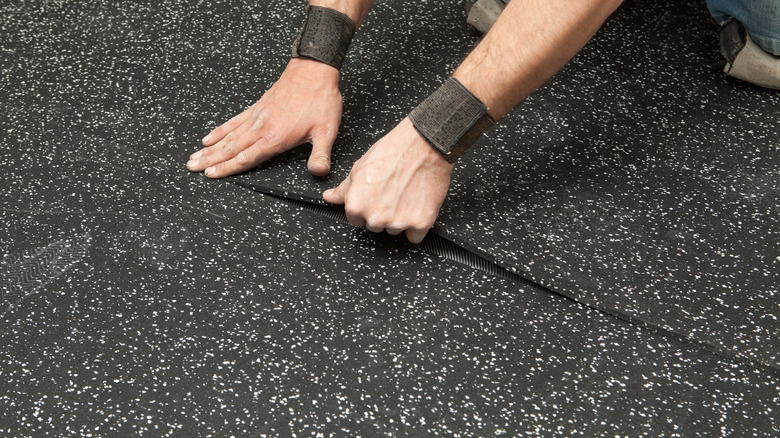 Man installing a black rubber floor in a room