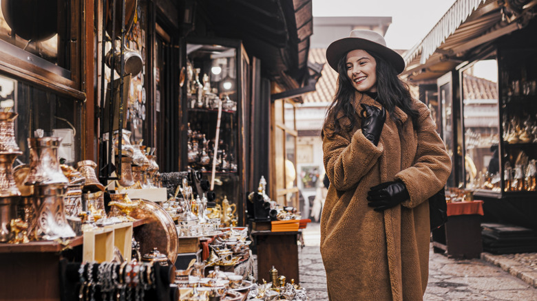 A woman in a fur coat smiles as she walks past an antique store