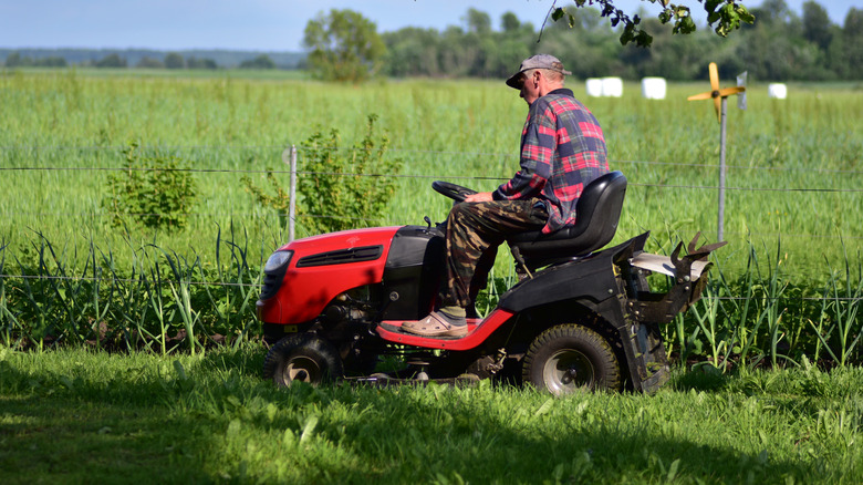 A man sits on a lawn mower on a sunny day