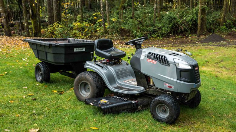 A grey-green lawn tractor with a dump cart in the grass