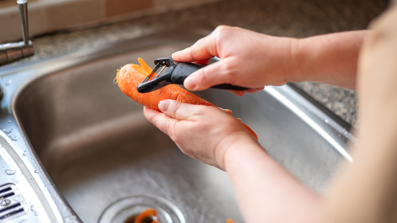 Hands using a peeler to remove the skin from a carrot