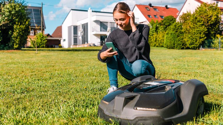 A woman using a smartphone next to a robot lawn mower
