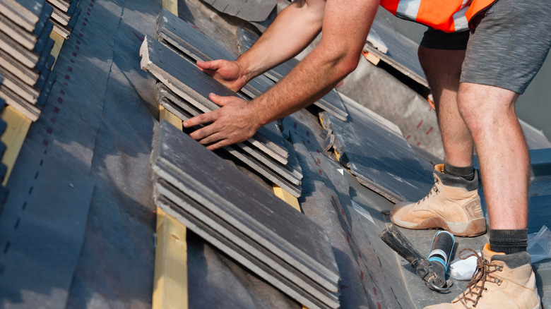 A worker replacing slate tiles on a roof.