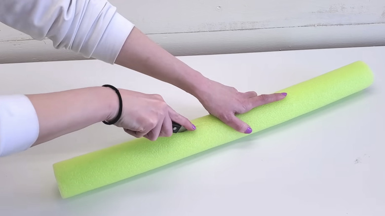 A person cutting a lime green pool noodle on a white table