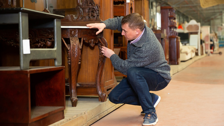 A man examines a wood table in a thrift store