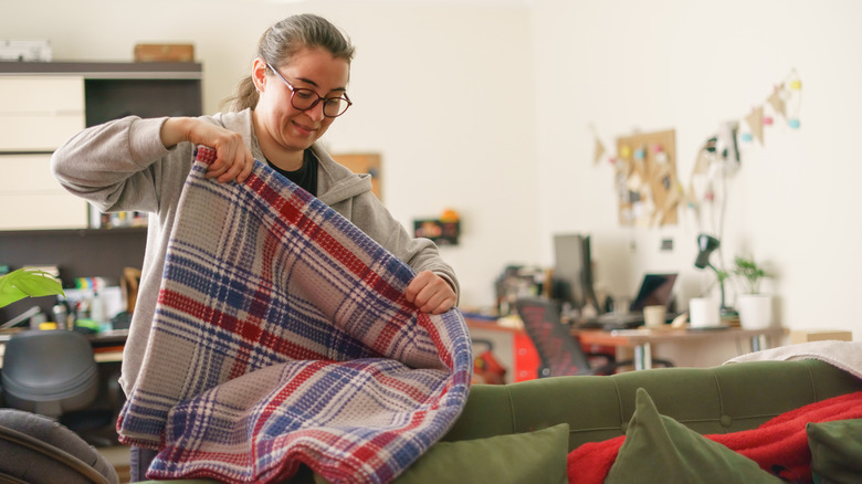 Woman folding up a large blanket above her couch