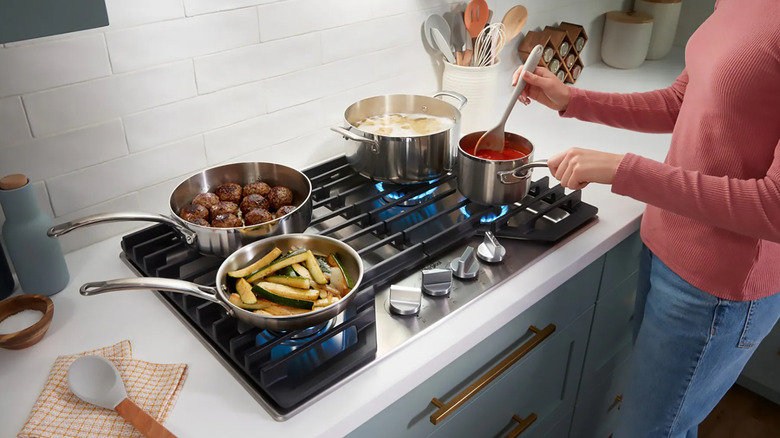 A woman cooking on a Whirlpool 30-inch 4-burner stainless steel gas cooktop with four pots going