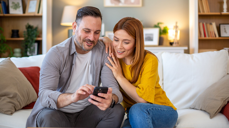 A woman smiles while her partner shows her something on his phone