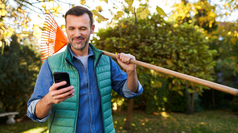 A person smiling at their phone while taking a break from yard work