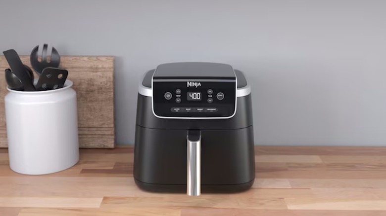 A Ninja Pro 5-Quart Black Digital 1-Basket Air Fryer sits on a wooden kitchen countertop next to a white crock full of utensils