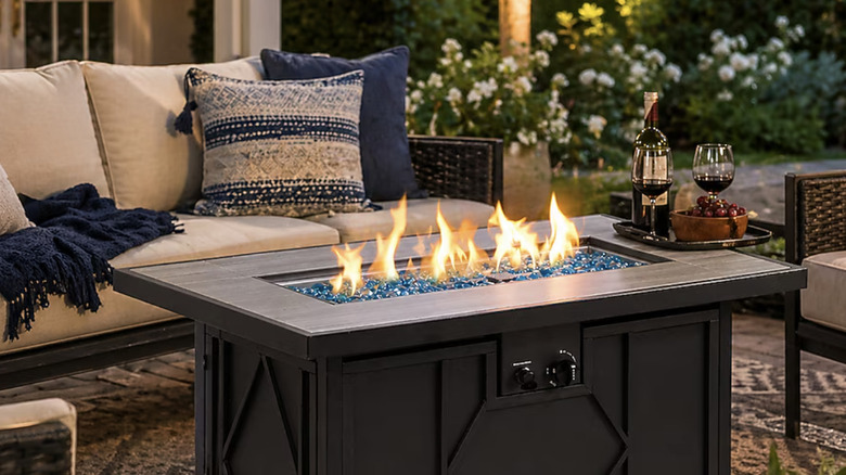 HEATMAXX 24-in Portable Liquid propane Fire table in the evening surrounded by cushioned furniture and holding wine and cheese plates