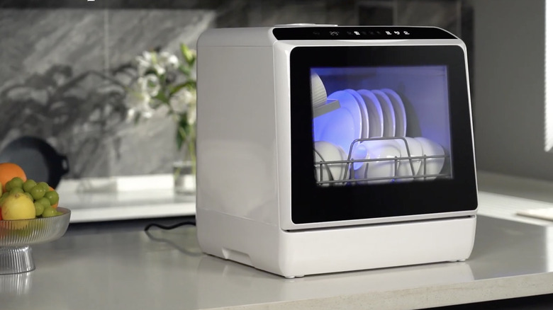 A portable dishwasher with white plates, bowls, and mugs on a countertop