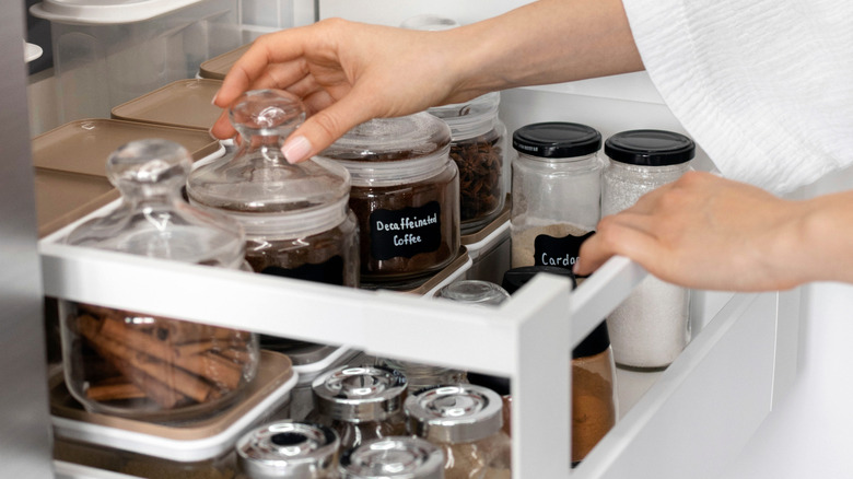 A woman puts spice jars into a cluttered drawer
