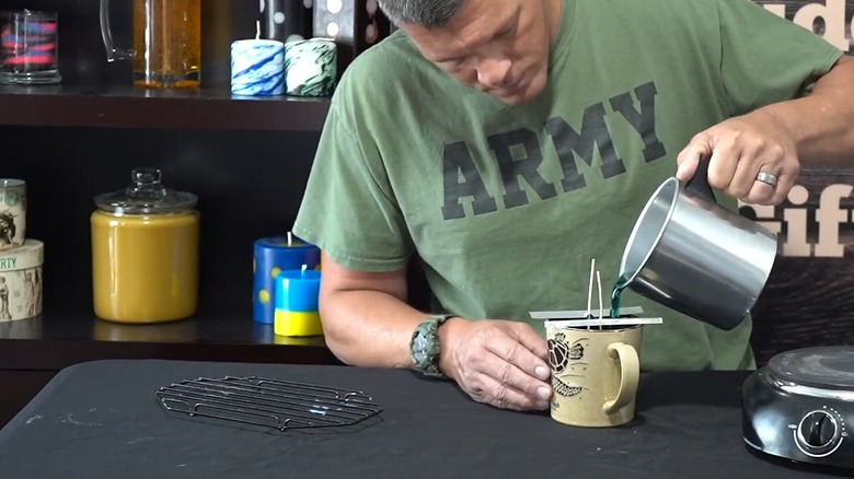 Man pouring melted wax in a coffee cup with wicks