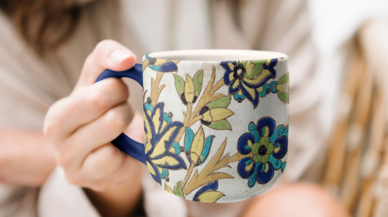 person holding floral painted vintage mug