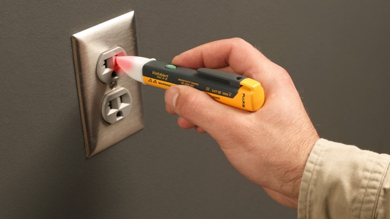 Person testing electrical receptacle with a non-contact voltage tester