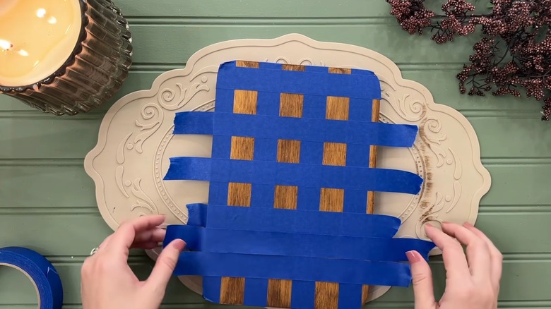 A person uses painter's tape to create a grid on a wooden cutting board