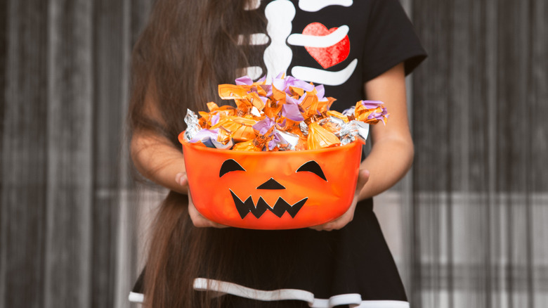 Woman in a skeleton costume holding a Halloween candy bowl