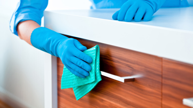person wearing rubber gloves and wiping down a wood cabinet with a cloth
