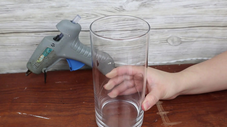 A person's hand holding a Dollar Tree glass vase on a table