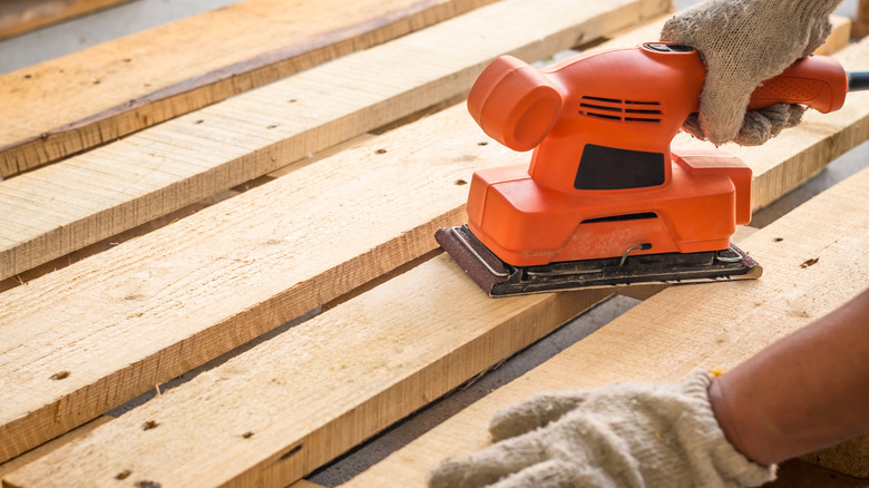 Man using a belt sander tool to prep a wooden pallet for a DIY