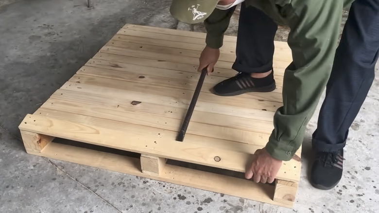 man prying plank from wood pallet