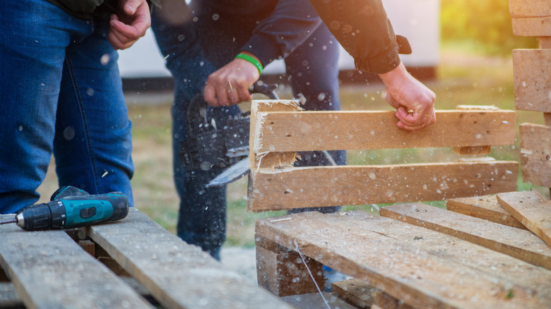Person sawing through a wood pallet