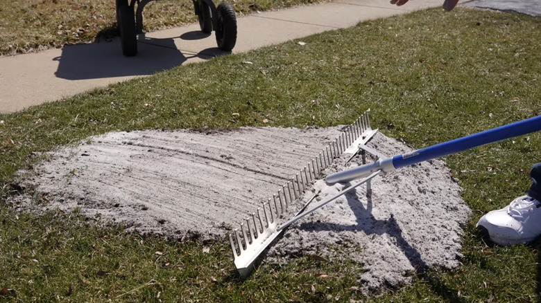 A person using a landscape leveling rake to smooth their lawn