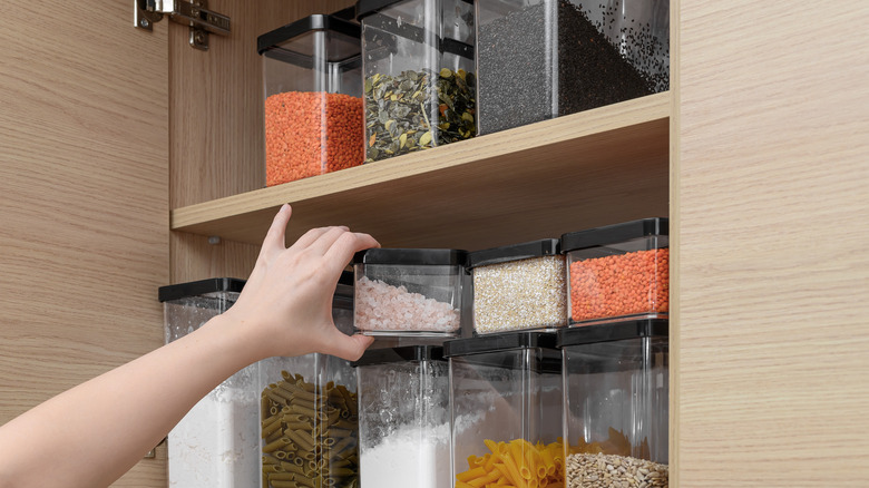 a hand reaches into a pantry filled with translucent boxes