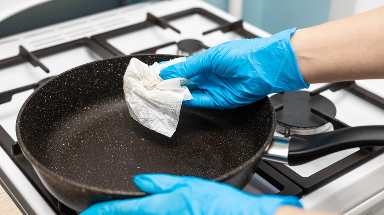 Gloved hand holding a paper towel above a pan