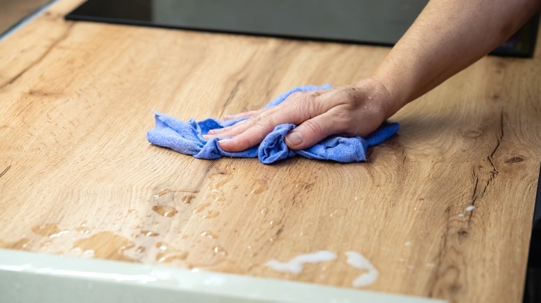 Person wiping down a water spill on a wood kitchen counter