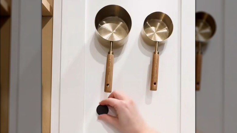 Person attaching magnets to cabinet door to hang metal measuring cup set