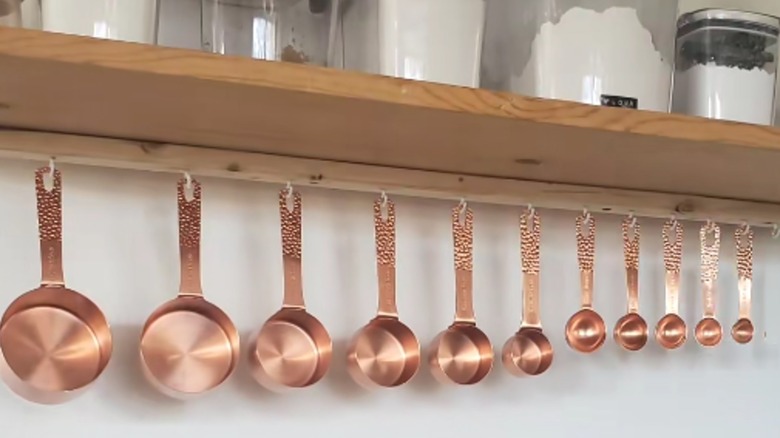 Red copper-style measuring utensils hanging from homemade wood rack under cooking ingredients