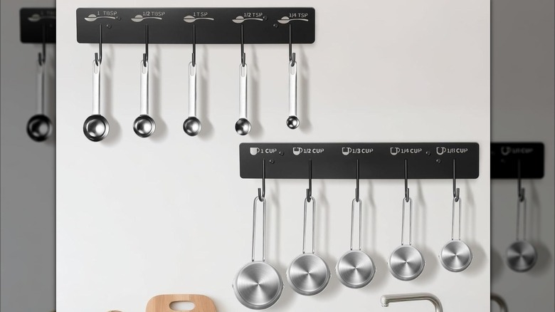 Stainless steel measuring cups hanging from decorative labeled rack on white wall