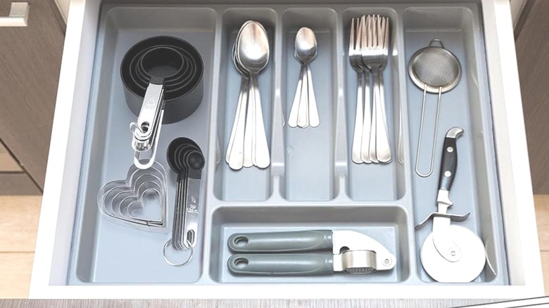 Stacked black and stainless steel measuring cup set in shallow drawer with plastic dividers