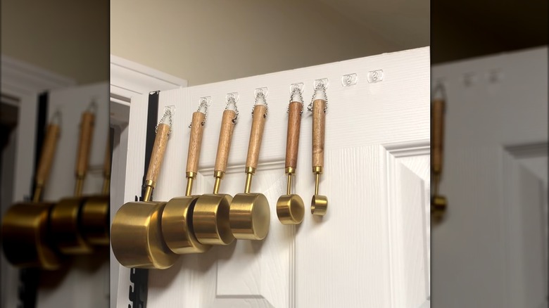 Stylish gold and wood handle measuring set hanging from command hooks and chains on white pantry door
