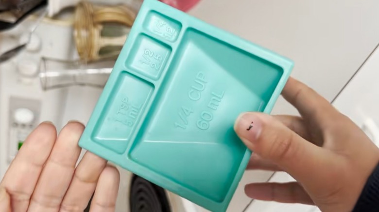 Person holding clean teal kitchen cube over white kitchen cabinets and drawers