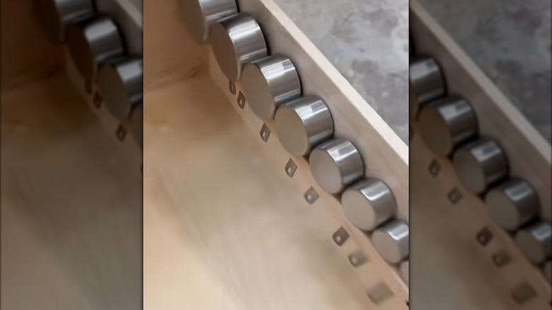 Metal measuring cups tucked in custom wood holder on kitchen drawer interior