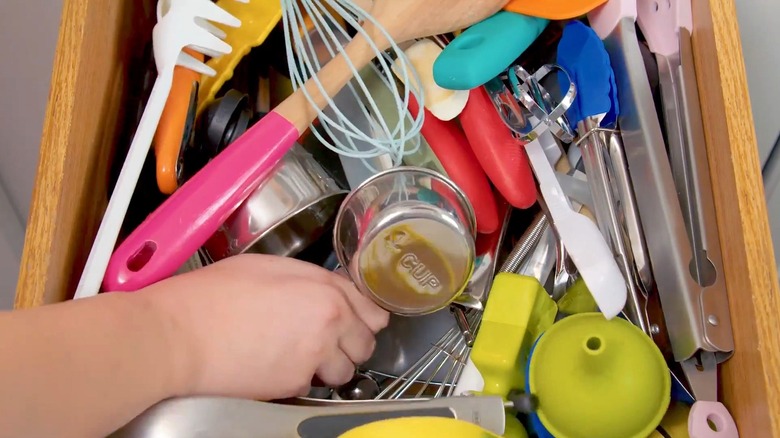 Person pulling measuring cup from a cluttered kitchen drawer