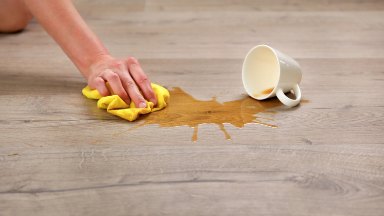 A person wiping up a coffee spill on laminate flooring.