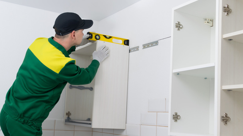 Man with gloves using a level while installing upper kitchen cabinets