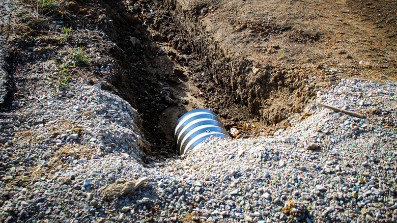 A drainage culvert pipe buried under gravel