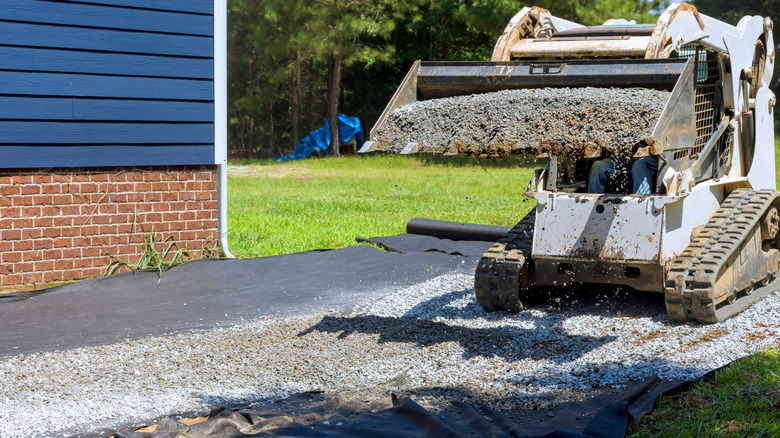 A Skidsteer installing a gravel driveway next to a house