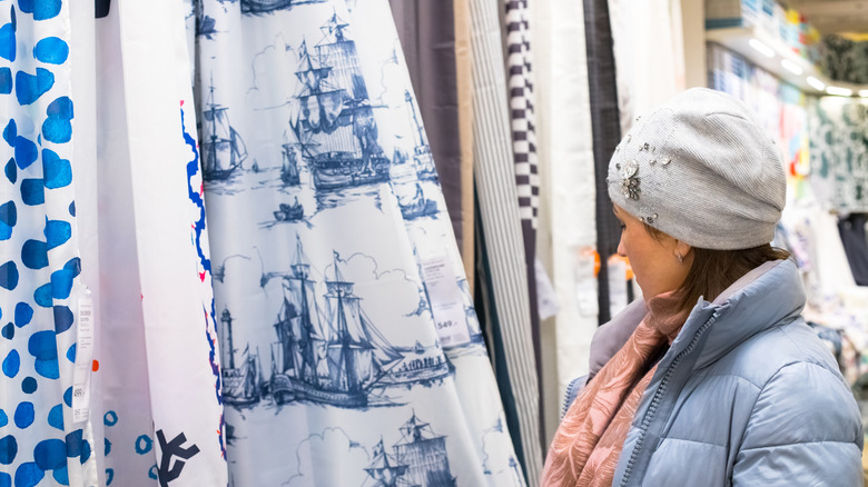 Woman shopping for stylish shower curtains hanging.