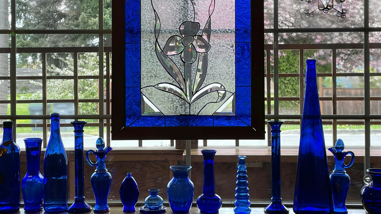 A stained and etched glass panel hanging in a residential window with matching glassware on the table below