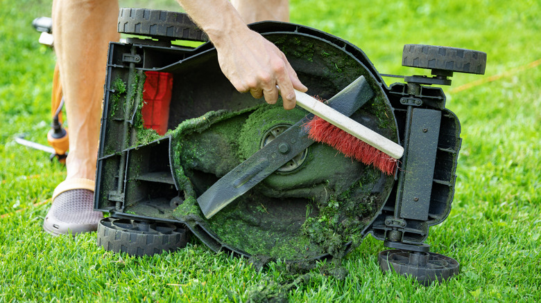 Man cleaning lawn mowed blades with brush
