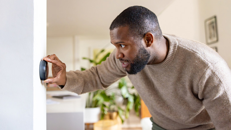 man in sweater adjusting thermostat
